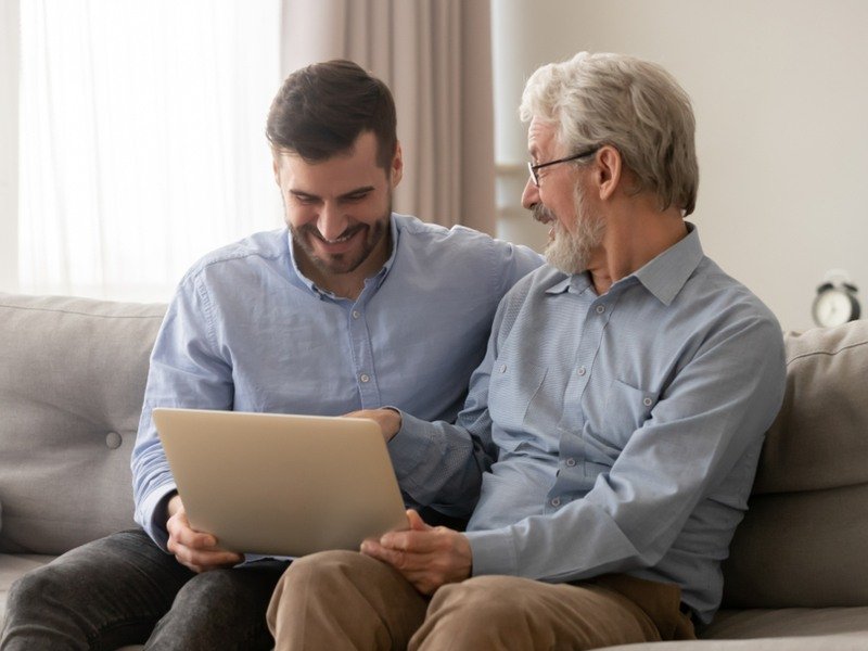 Padre anziano e figlio adulto seduti sul divano mentre usano un laptop